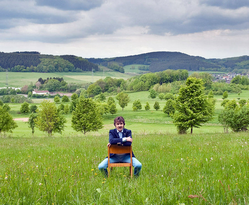 Peter Guntermann sitzt auf Stuhl vor Sauerland Panorama - verwurzelt im Sauerland