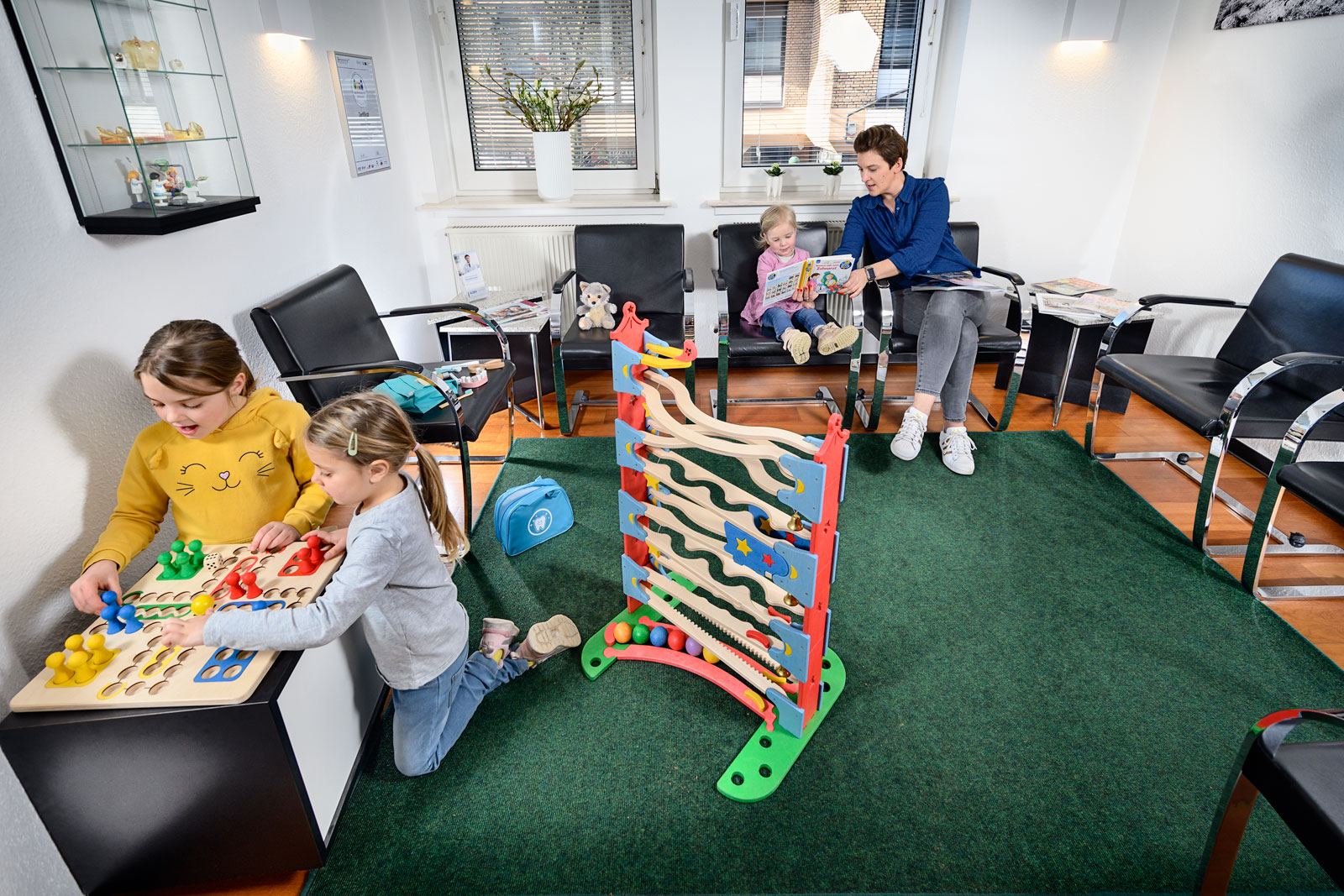 Wartezimmer - zwei Kinder spielen Mensch Ärger dich nicht und Mutter liest Kleinkind aus Buch vor - Zahnarzt und Fachzahnarzt Praxis Guntermann, Olpe. Foto Dietrich Hackenberg