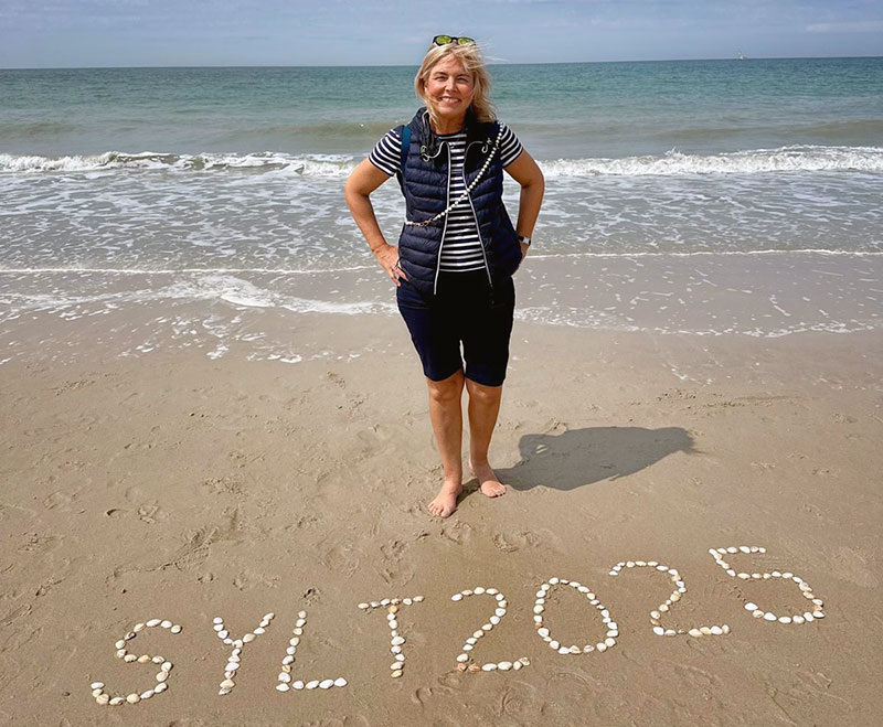 Frau am Strand mit Muschelschriftzug "Sylt 2025"