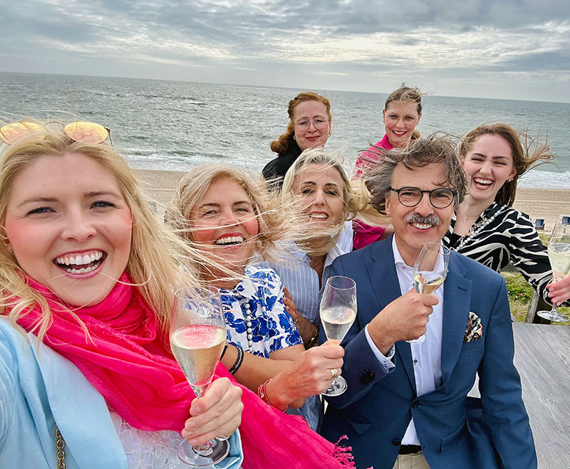 Praxisteam am Strand in Sylt mit Sektgläsern - im Hntergrund das Meer