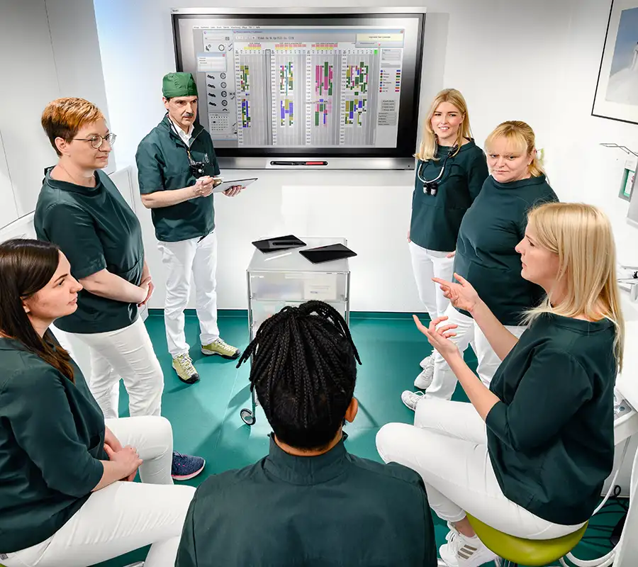 Besprechung des Praxisteams in einer Runde vor dem Smartboard an der Wand