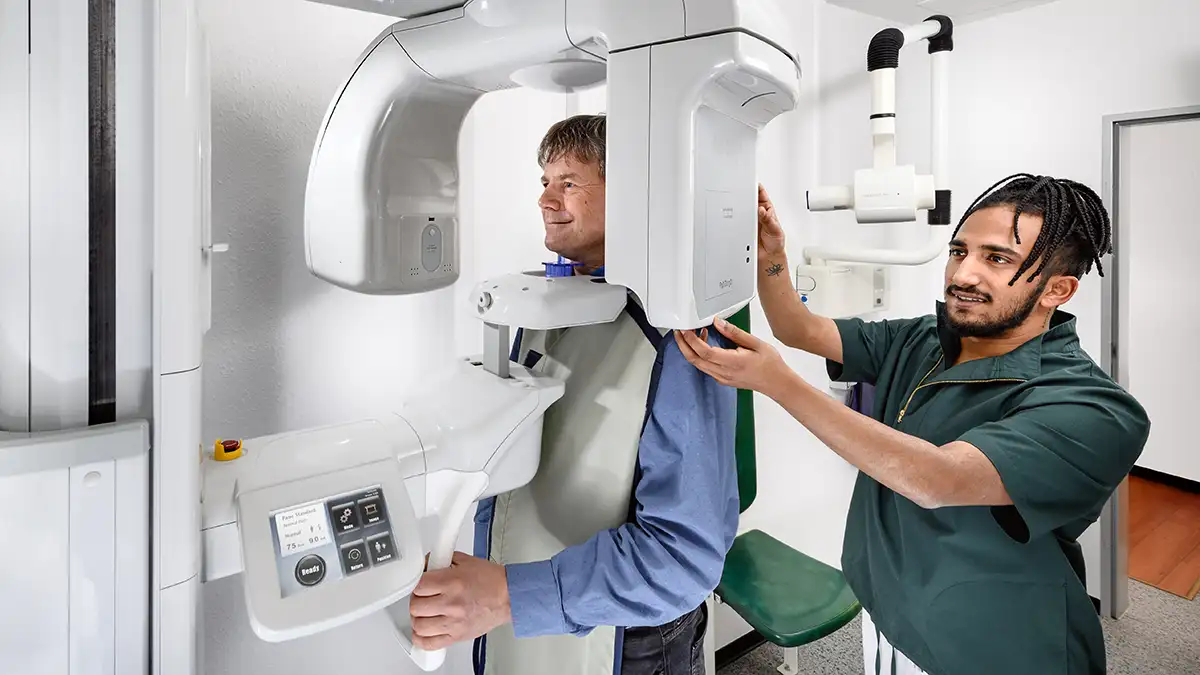 Helfer mit geflochtenen Haaren stellt Digitalen Volumentomograph ein an dem ein Patient steht