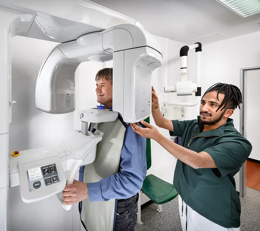 Helfer mit geflochtenen Haaren stellt Digitalen Volumentomograph ein an dem ein Patient steht